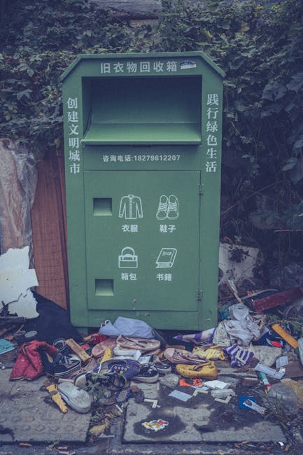 A black wheeled rubbish bin labeled 'St. John's' positioned on a residential street at night, with its lid open and filled with various discarded waste items including cardboard and plastic trash bags